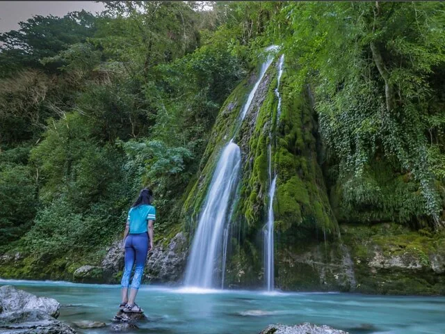 Woman standing on a rock looking at a mossy waterfall