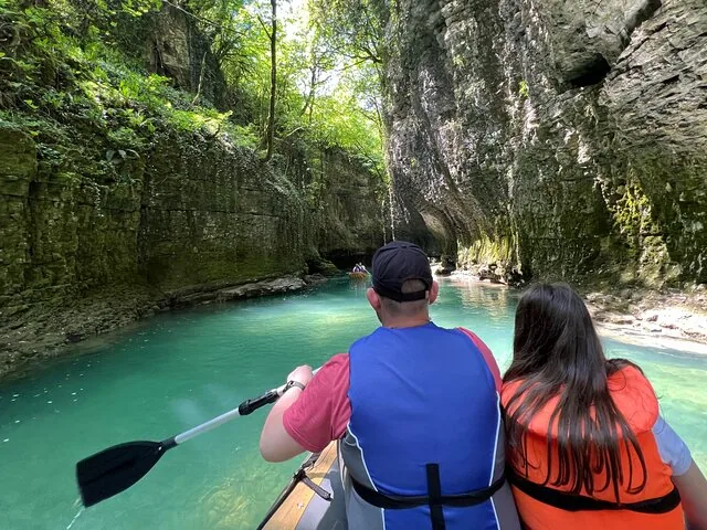 Two people kayaking on a bright blue river in a lush green canyon