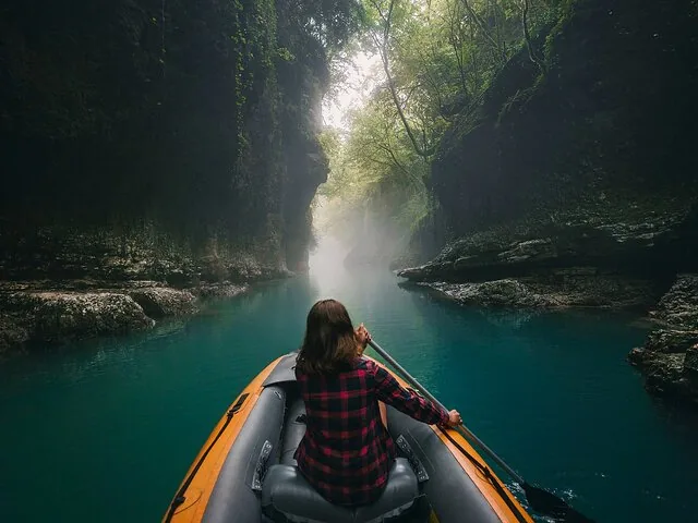 Person in a yellow inflatable boat rowing through a narrow, misty canyon