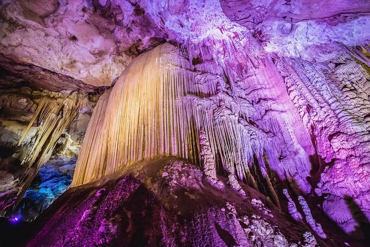 Große spektakuläre Stalaktitenformationen, die in einer Höhle mit violettem und blauem Licht beleuchtet werden