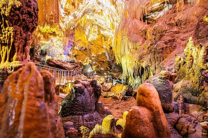 Intérieur de la grotte de Prométhée montrant de grandes stalagmites, des stalactites et une passerelle en bois