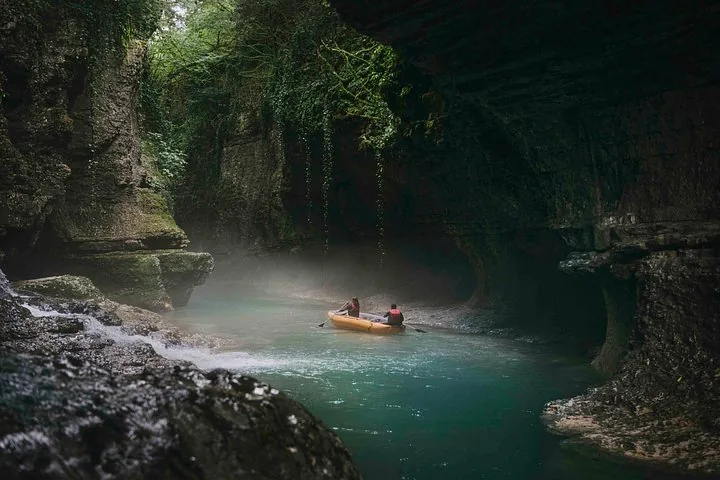Zwei Personen paddeln mit einem Schlauchboot auf einem Fluss in einer felsigen Schlucht