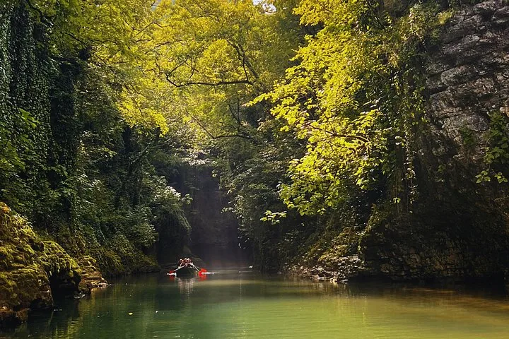 Small boat with people navigating a river inside Martvili Canyon
