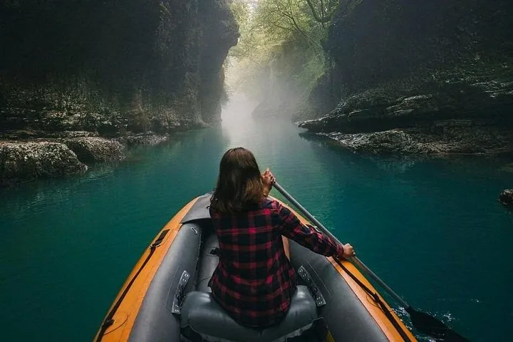 Persona che pagaia su una barca in un fiume verde e nebbioso attraverso un canyon
