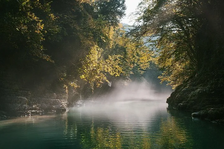 Fiume verde e nebbioso che scorre attraverso un canyon lussureggiante con la luce del sole che filtra